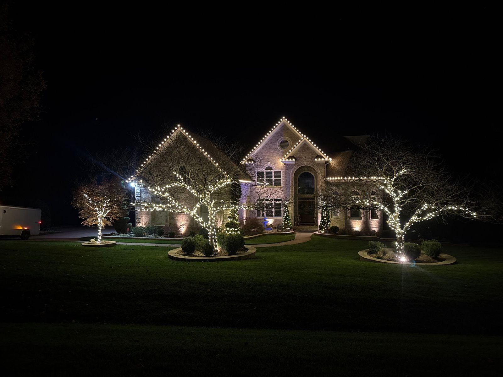 Christmas light installation in Raleigh, NC with warm white roofline lights, light-wrapped trees, and landscape uplighting across the front yard