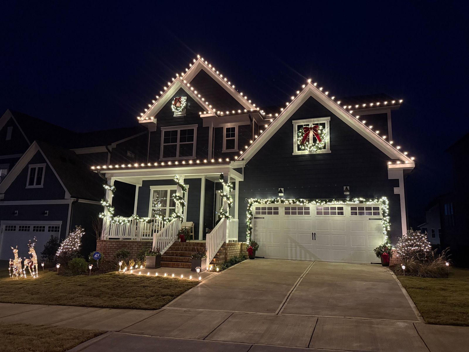Residential Christmas light installation in Raleigh, NC with warm white roofline lights, lit wreaths, porch garland, and pathway lighting