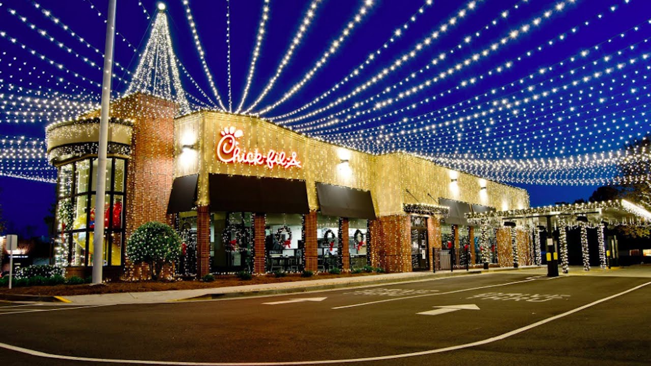 Commercial Christmas lighting installation at a restaurant storefront in Raleigh, NC with overhead radiating string lights, lit brick facade, and wreaths on the columns