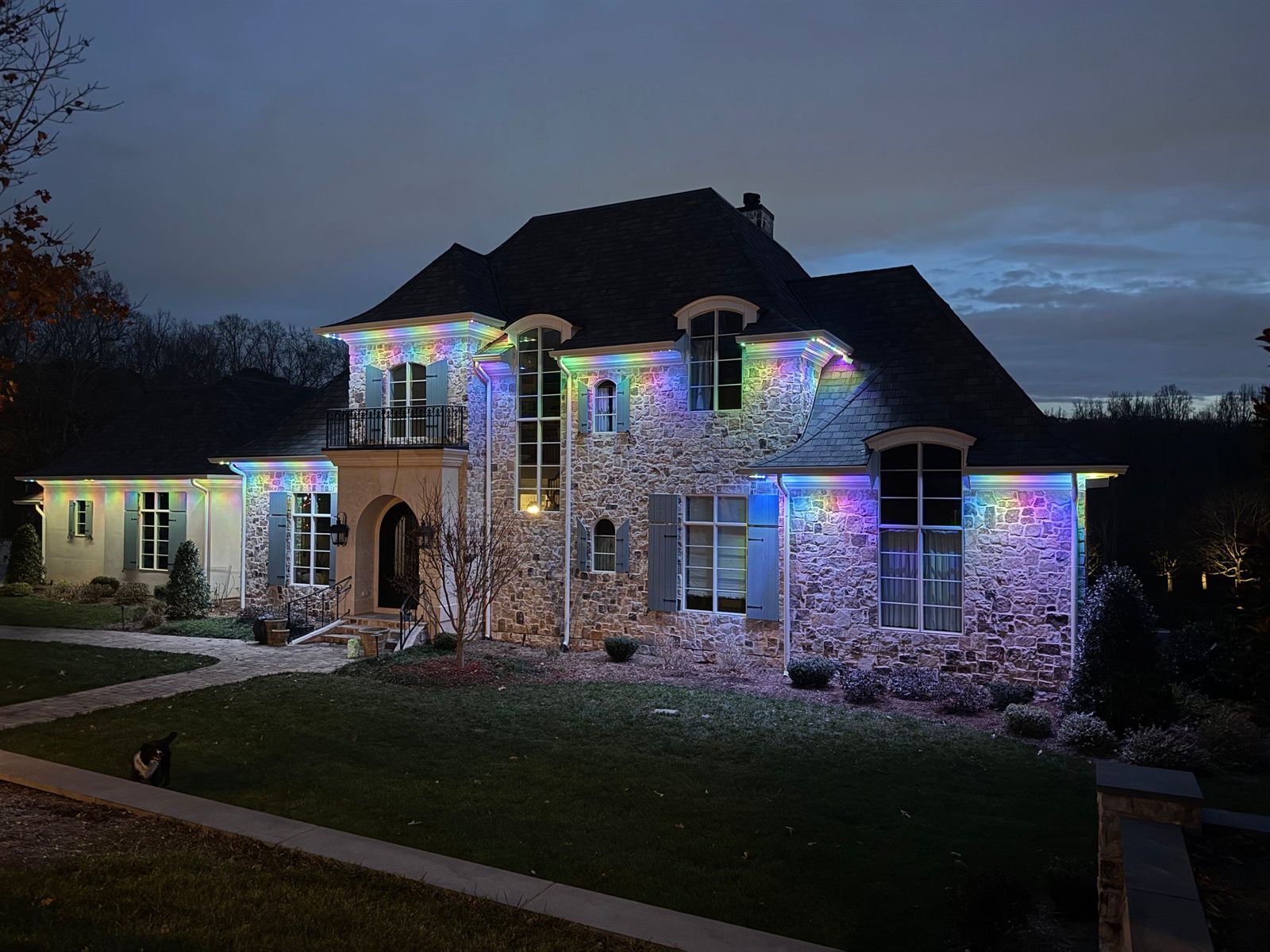 Permanent color-changing LED lighting washing the stone facade and rooflines of a large home in Raleigh, NC at dusk